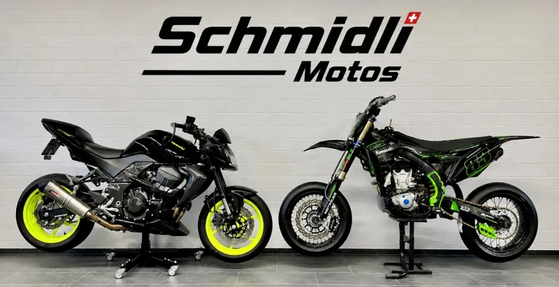 Showroom-Wand mit dem Schriftzug Schmidli Motos, davor eine schwarze Kawasaki Z mit neongelben Felgen und eine grün-schwarze Supermoto.